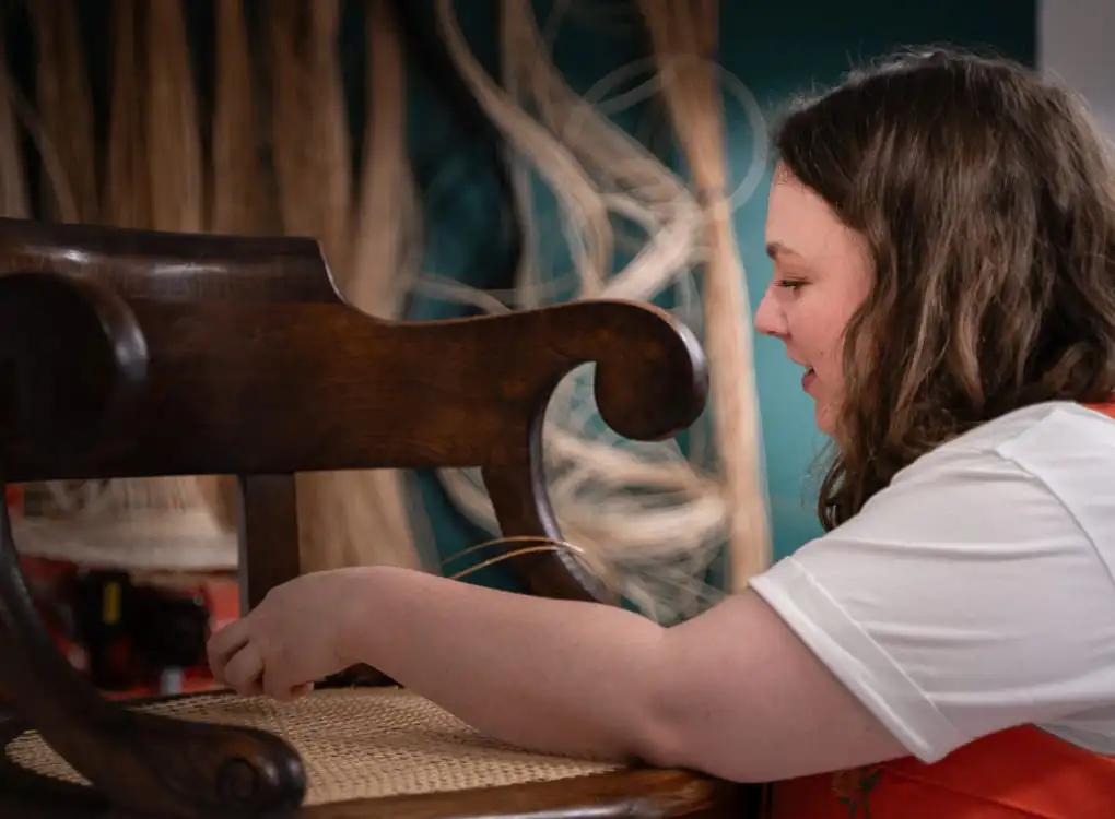 Inès Hayaud en train de restaurer une fauteuil de Maire en cannage  de manière traditionnel. Photo prise dans son atelier par Nathalie Rodriguez